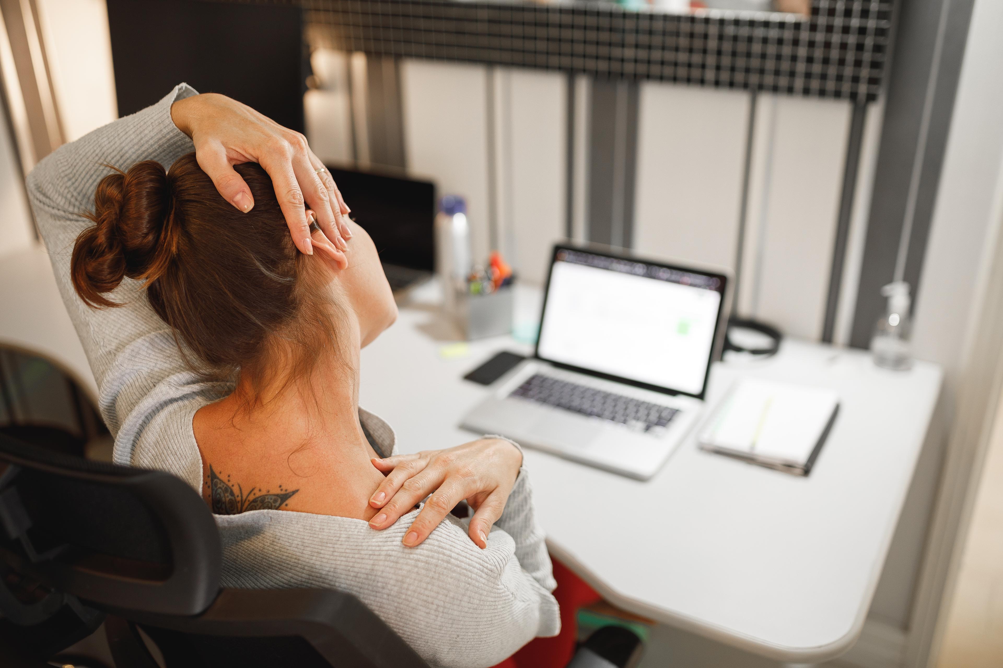 Kvinna som sitter vid datorn och stretchar nacken