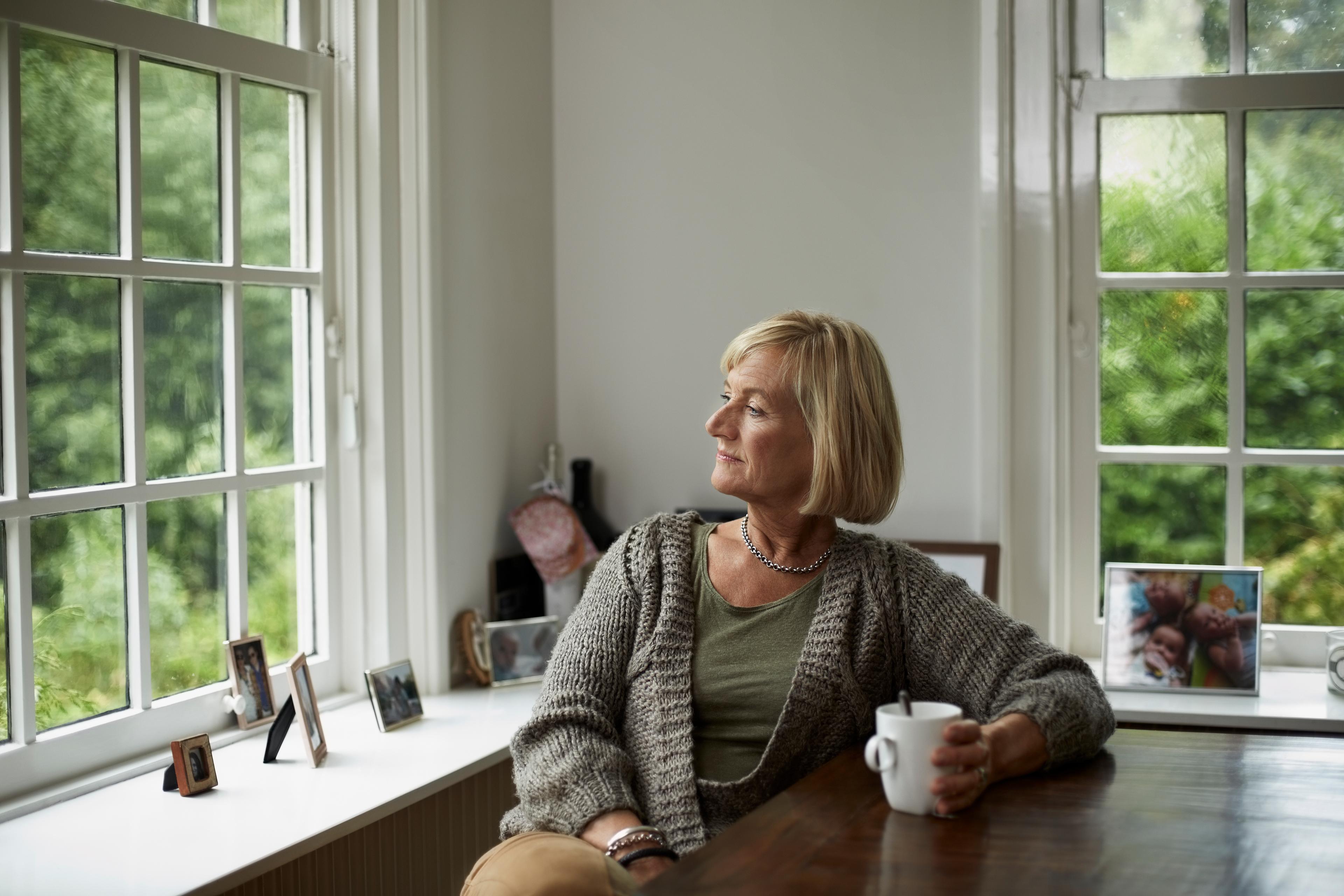 En kvinna sitter och dricker kaffe och blickar ut genom fönstret
