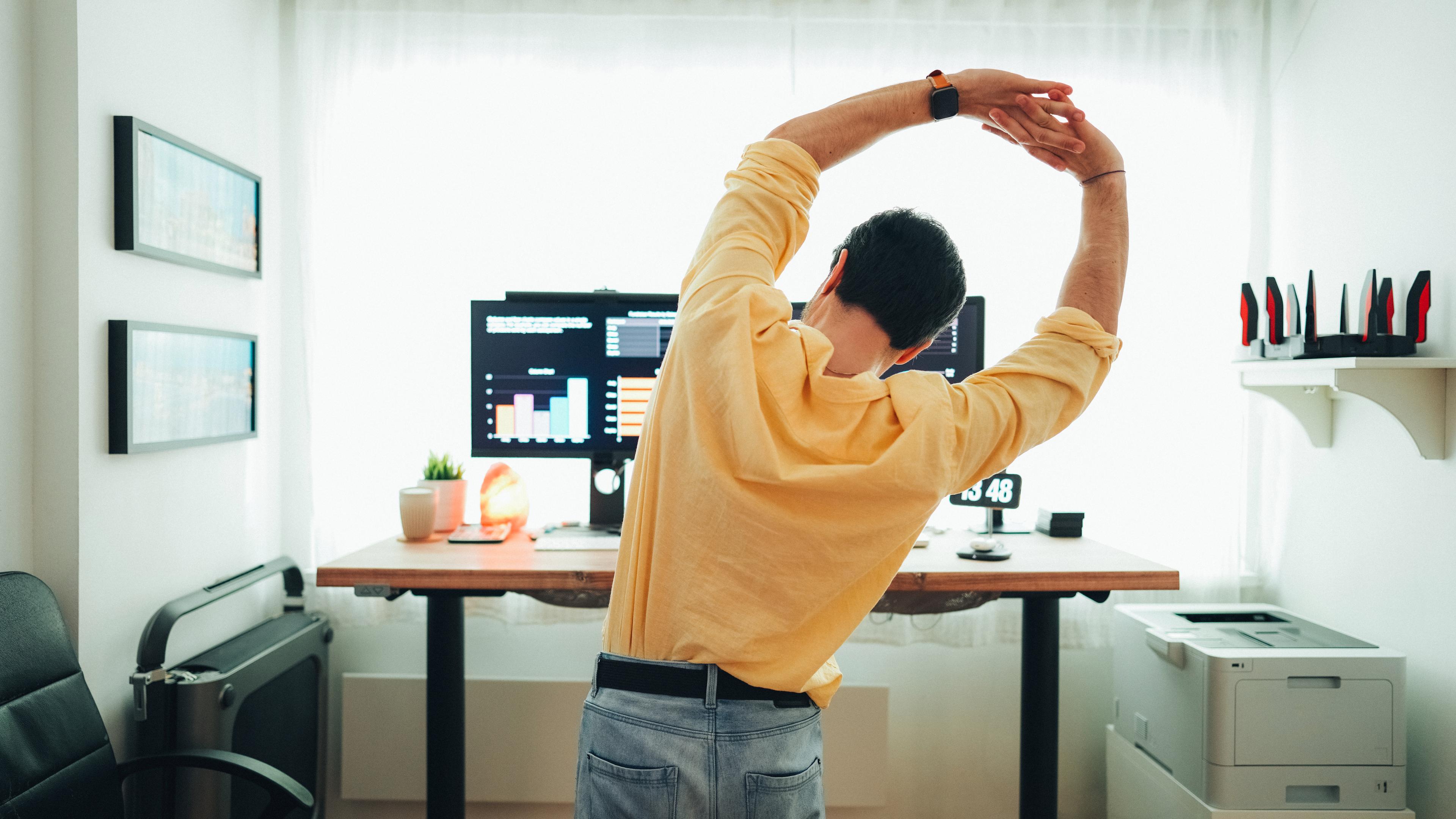 En man står fram datorn och stretchar