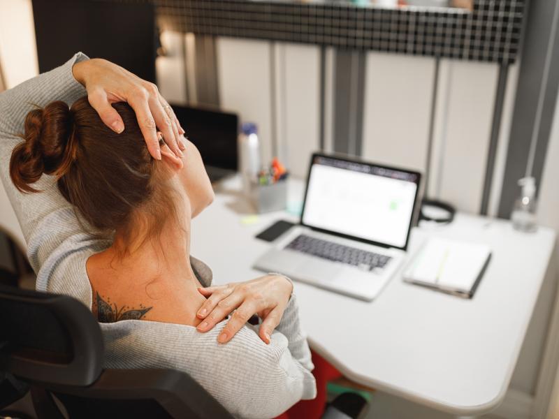 Kvinna som sitter vid sin dator och stretchar nacken